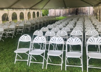 Rows of white chairs on a lawn under a white tent.
