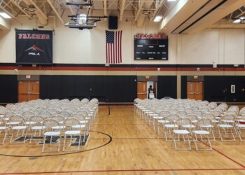 Rows of white chairs in a school gym.
