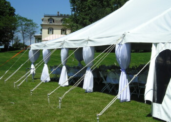 OLYMPUS DIGITAL CAMERA White outdoor event tent with round tables and chairs is set up on a grassy lawn near a house.