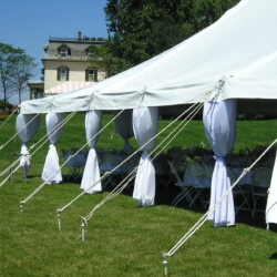OLYMPUS DIGITAL CAMERA White outdoor event tent with round tables and chairs is set up on a grassy lawn near a house.