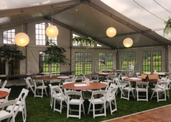 An event set up on a lawn under a tent with round tables and a dance floor.