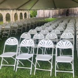 Rows of white chairs on a lawn under a white tent.